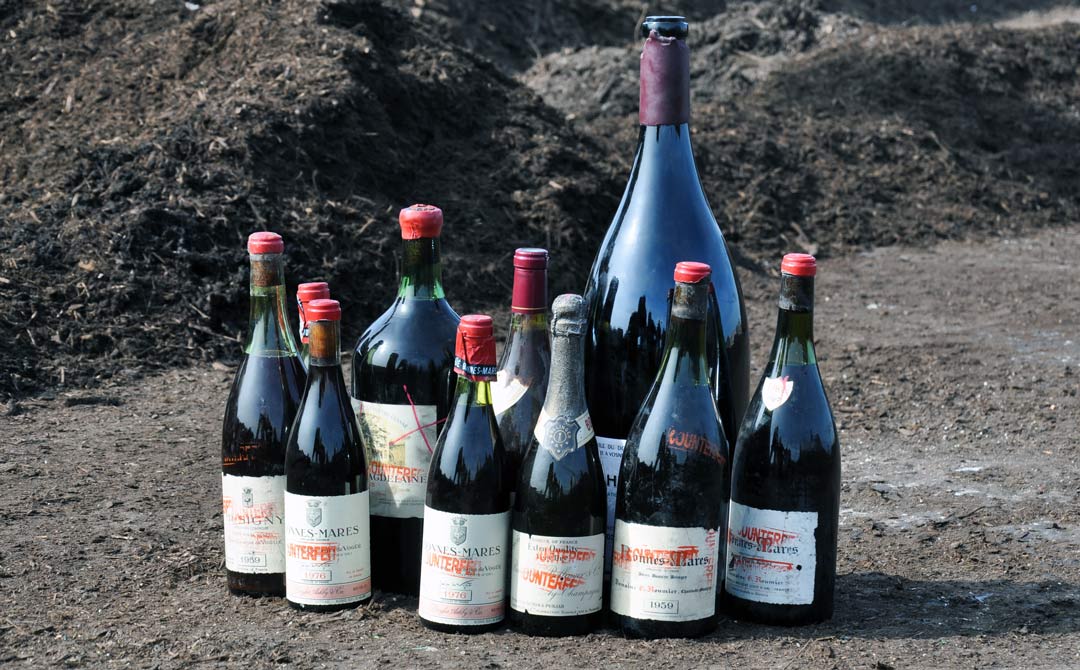 Line-up of seized counterfeit wine bottles marked with red paint and labels reading “counterfeit”